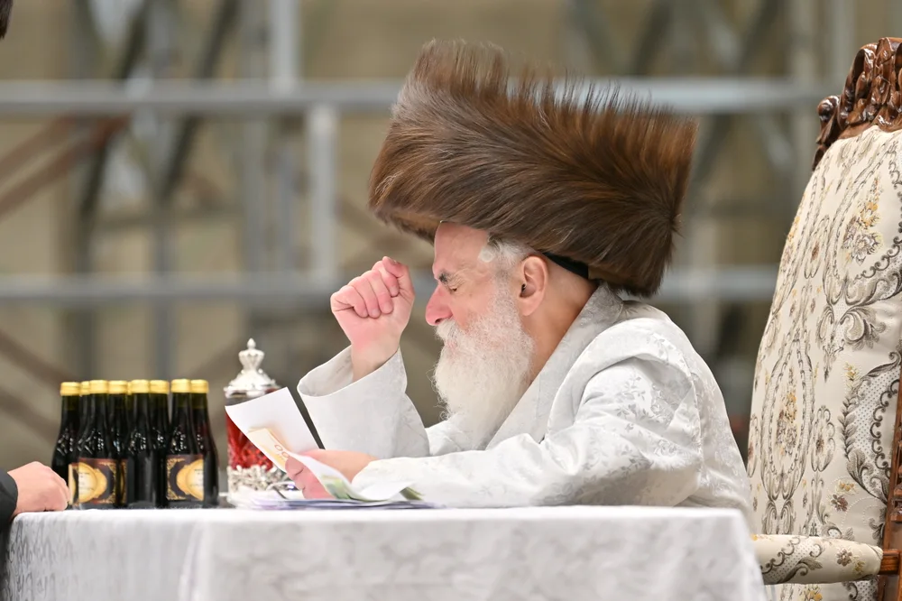 The Viznitzer Rebbe seated at his table, holding a kvittel